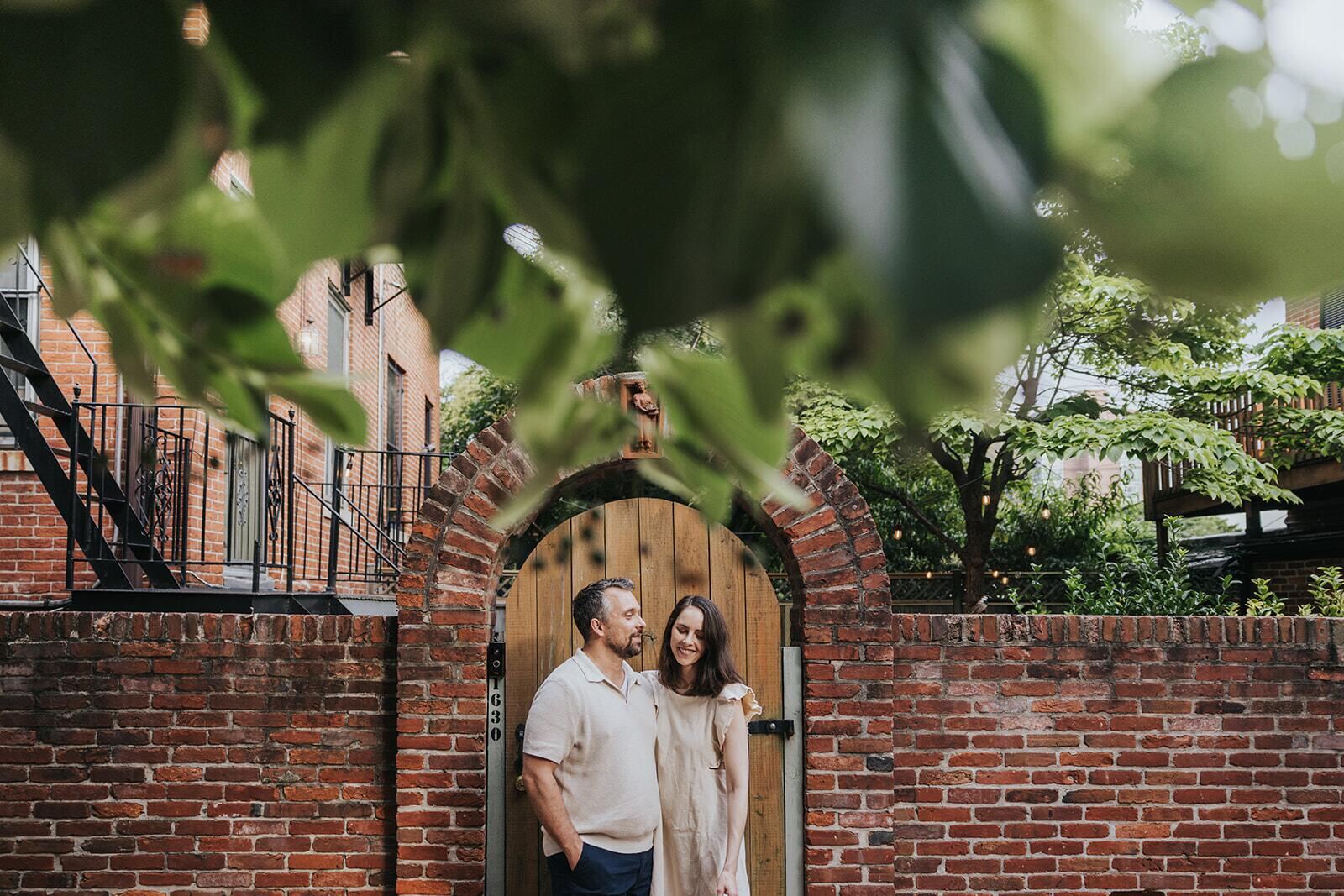 Ben and Shannon standing together in the arched brick gateway of a Baltimore garden wall