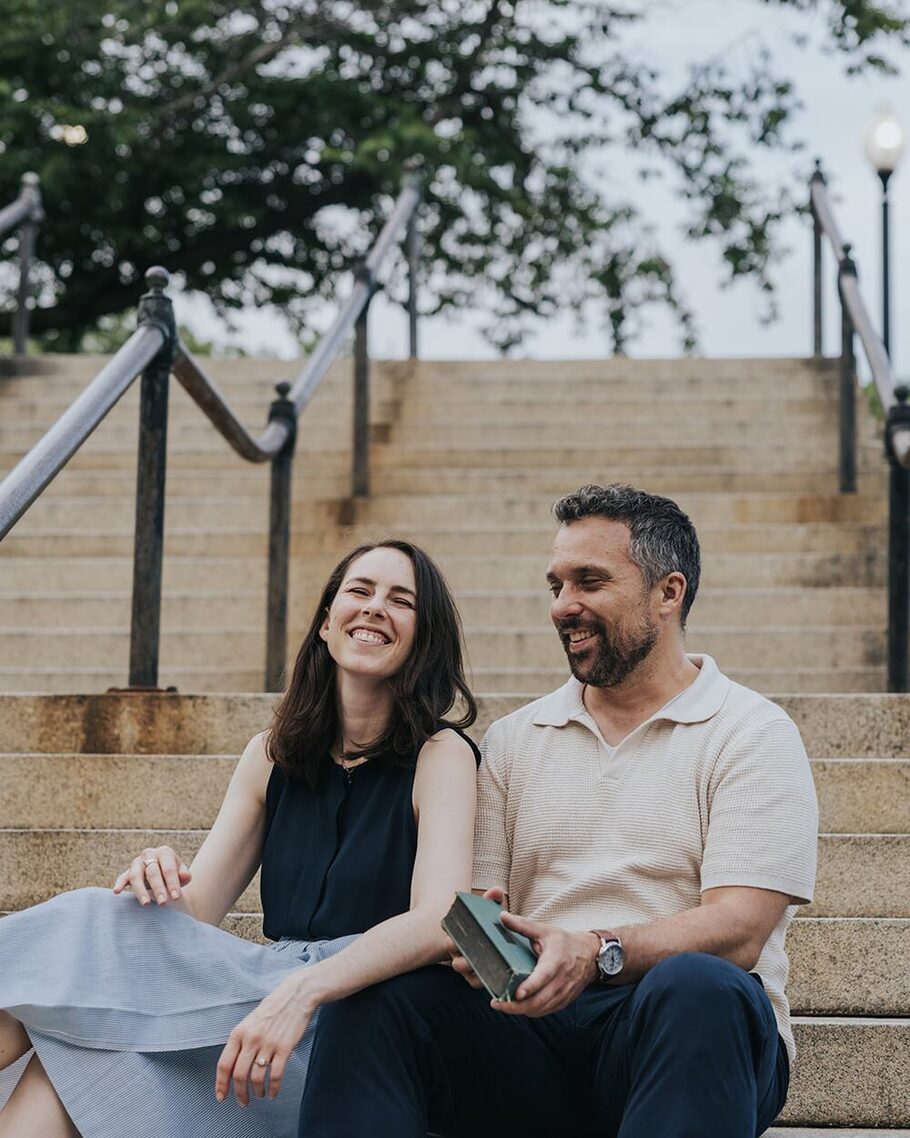 Ben and Shannon sitting on a flight of stone steps, laughing together on a summer afternoon