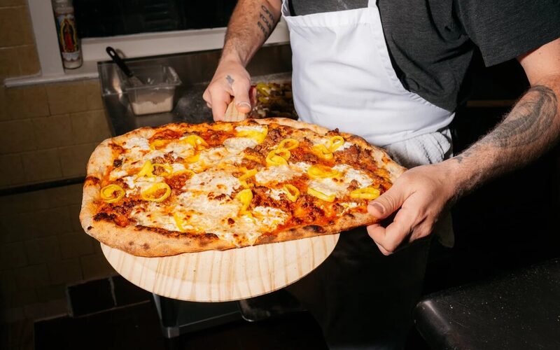 A cook carrying a just-baked pizza on a wooden peel at Little Donna's