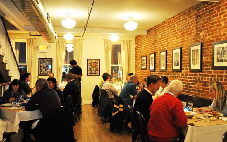 The upstairs dining room at Thames Street Oyster House, with exposed brick and white tablecloths